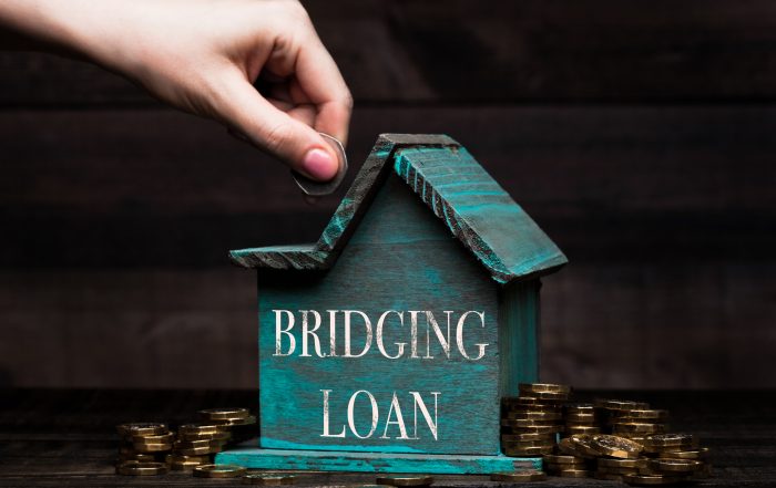 Wooden house model with coins next to it and hand Understanding Bridging Loan Interest Rates and Costs in Singapore