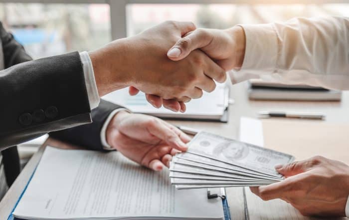 Corruption and Bribery ,Businessman shaking hands giving dollar Understanding Licensed Moneylenders in Singapore