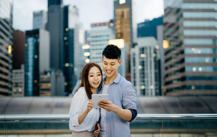 young-couple-using-digital-tablet-smartphone-city-against-modern-city-skyline-urban-terrace